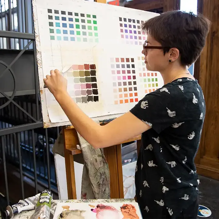 Female student paining a grid of color swatches.