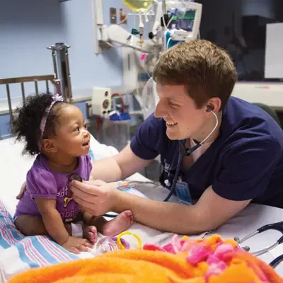 Male nursing student using a stethoscope to care for a toddler child.