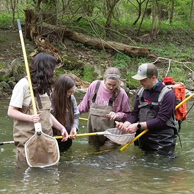 Professor and students wearing waders performing science experiments waist deep in a river.